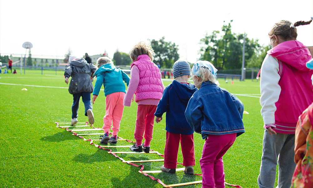 Children playing a stepping game on a grassy field at school.